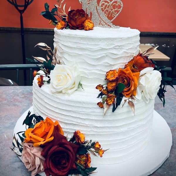 Two-tier white wedding cake with textured frosting, adorned with orange, red, and white flowers.