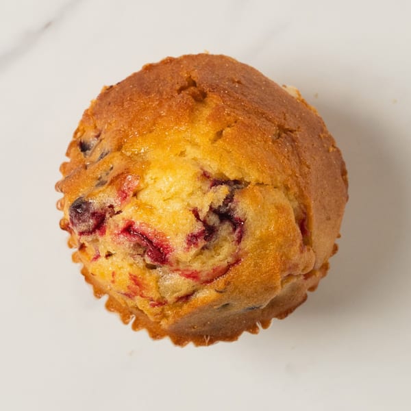 A golden-brown Elmwood Pastry Shop muffin with visible red and purple berries on a white surface.