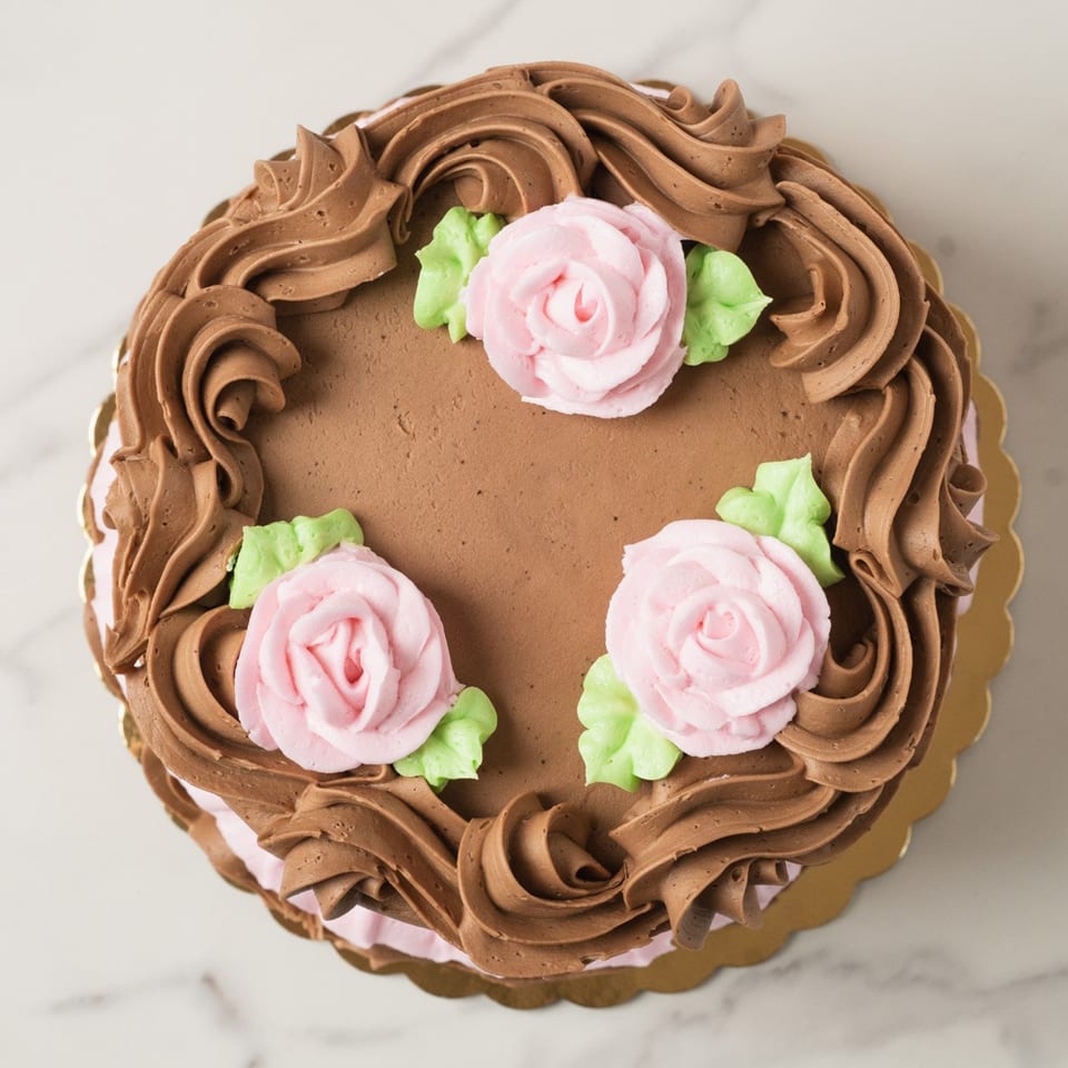 Elmwood Pastry Shop chocolate cake with pink buttercream roses and green leaves on a gold scalloped base.