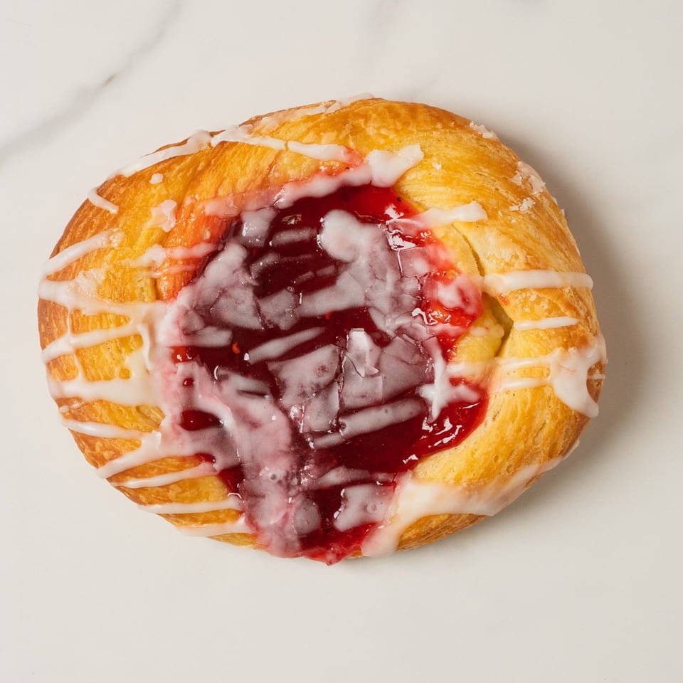 A golden-brown Elmwood Pastry Shop danish with a vibrant red fruit filling and white icing drizzle.