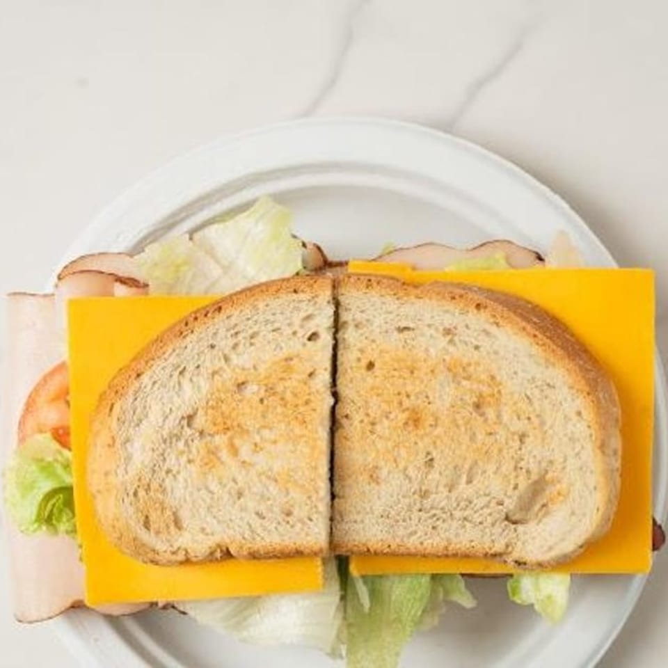 Toasted turkey and cheese sandwich with lettuce and tomato on a white plate.