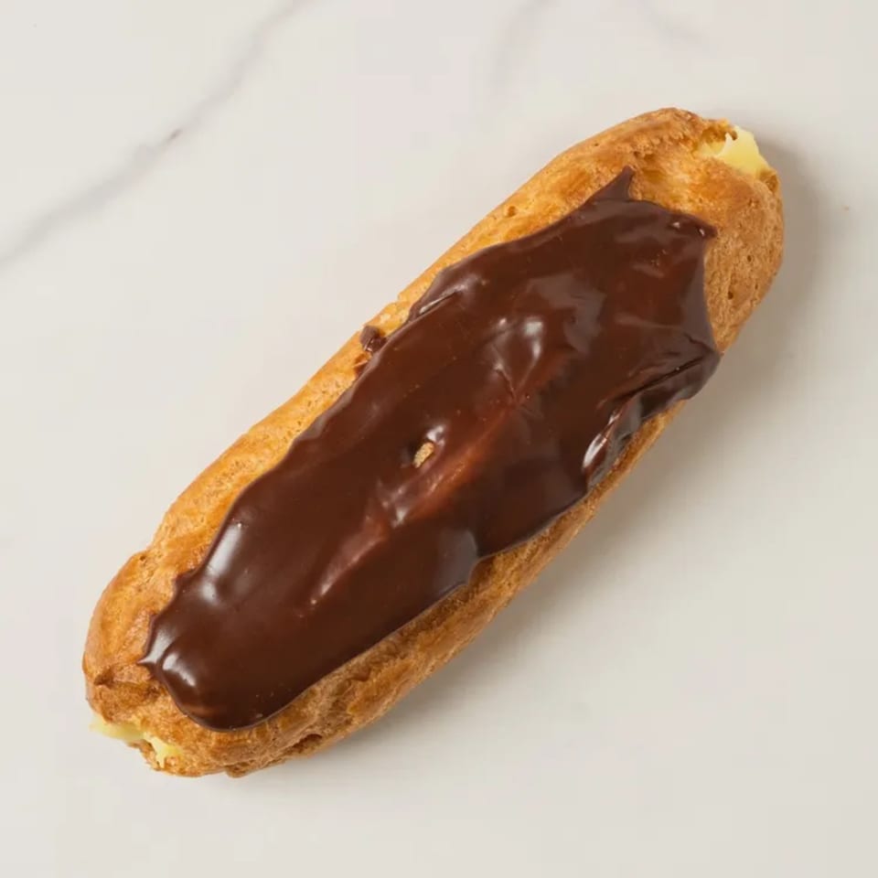 Elmwood Pastry Shop's chocolate eclair with creamy filling on a white marble surface.