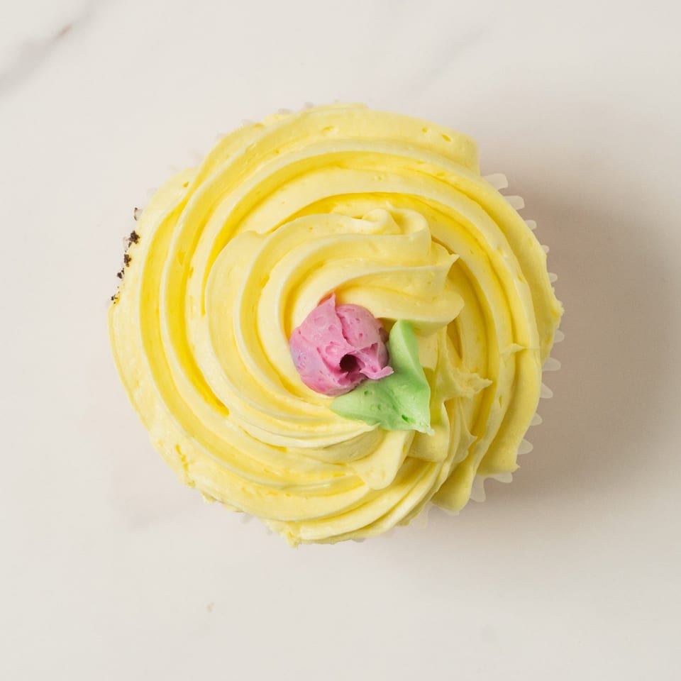 Elmwood Pastry Shop's yellow frosted cupcake with a pink and green flower decoration on top.