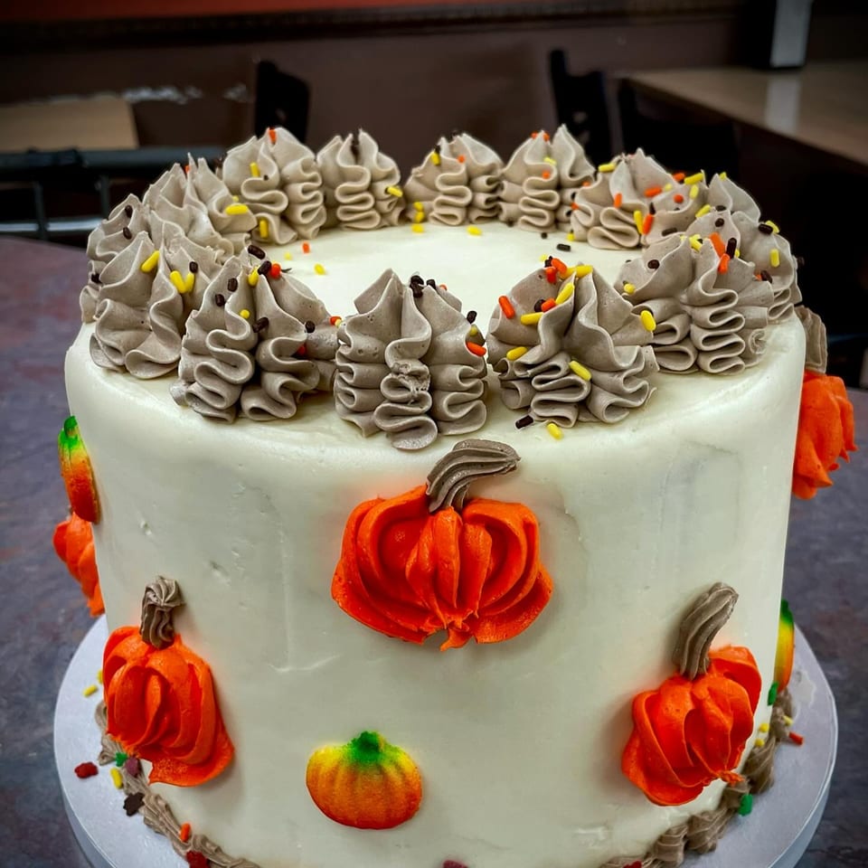 A white frosted cake with orange pumpkin decorations and brown and orange sprinkles.