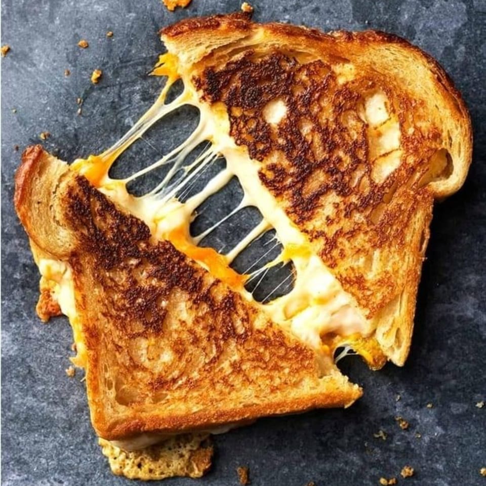 A grilled cheese sandwich, cut in half, with melted cheese stretching between the halves.
