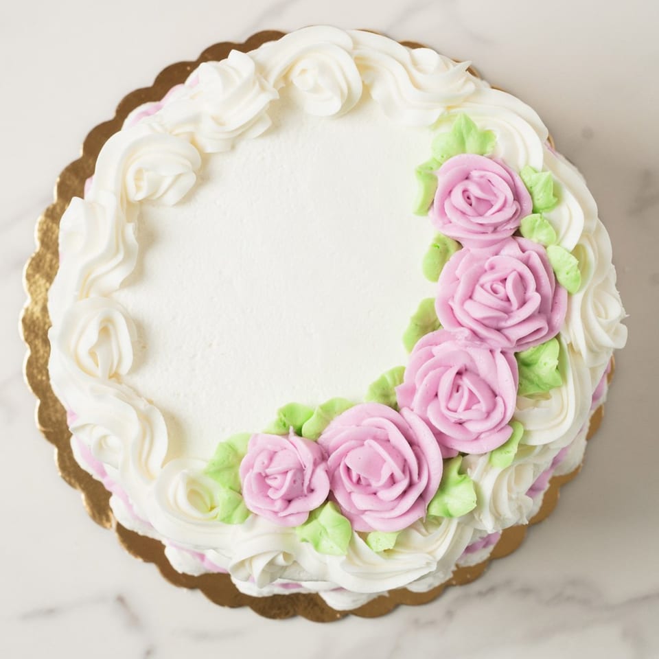 Elmwood Pastry Shop's round white cake with pink frosting roses and green leaves on a gold scalloped base.