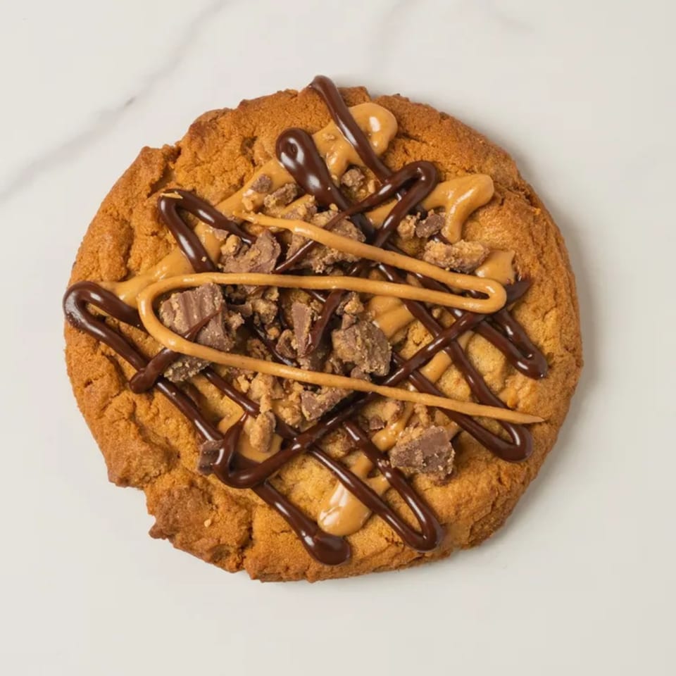 A peanut butter cookie from Elmwood Pastry Shop, drizzled with chocolate and peanut butter, topped with candy pieces.